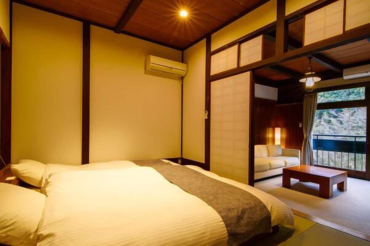 Ein traditionell gestaltetes japanisches Schlafzimmer mit Bett, einem kleinen Tisch und einer Schiebetür, die auf einen Balkon führt.