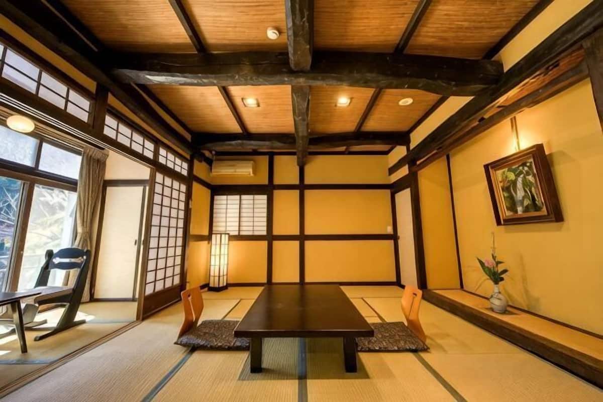 Ein traditioneller japanischer Raum mit Tatami-Böden, einem niedrigen Tisch, Schiebetüren und einem gerahmten Bild an der Wand.