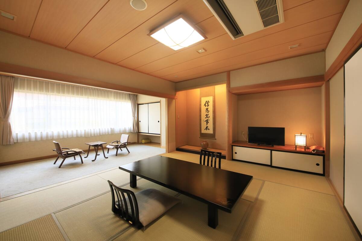 A traditional Japanese room with tatami flooring, a low table, and a television on a cabinet.