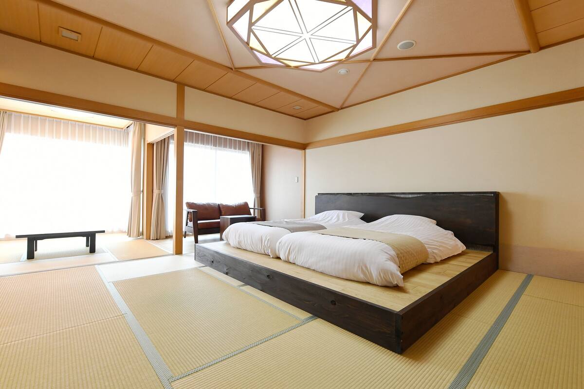 A traditional Japanese-style bedroom with tatami flooring, a low platform bed, and a wooden ceiling with a skylight.
