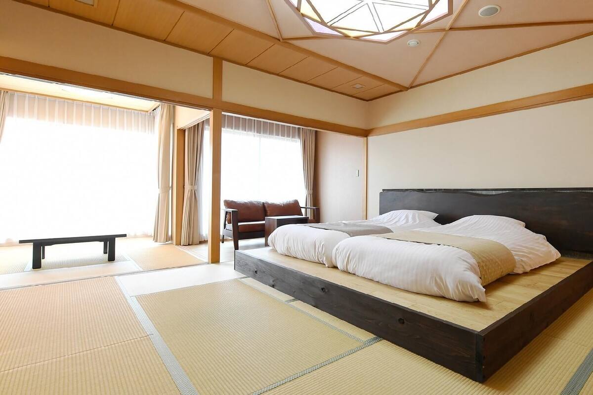 A traditional Japanese-style room with tatami flooring, a low platform bed, a bench, and a sliding door.