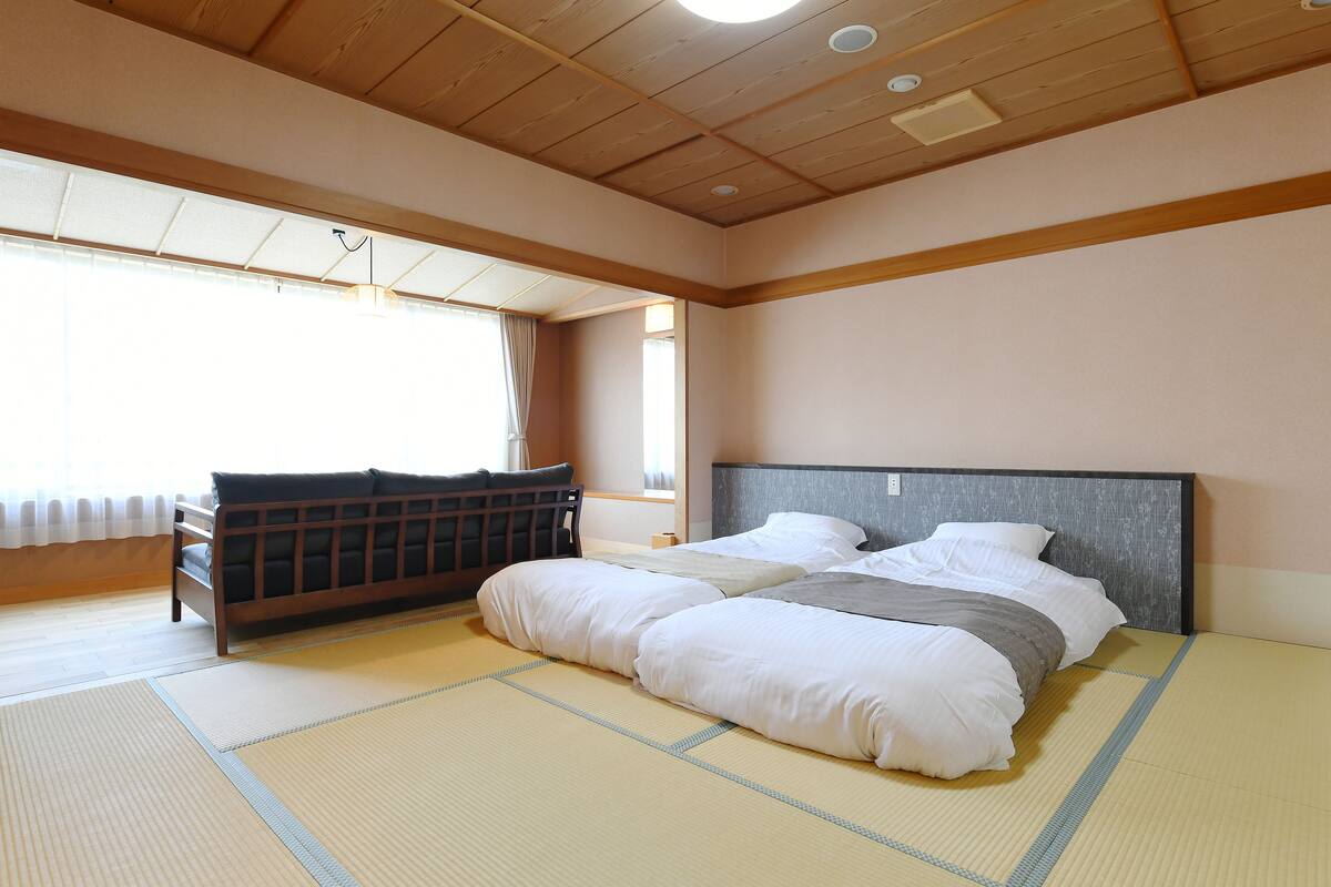 A traditional Japanese-style room with tatami flooring, a futon bed, and a wooden headboard.