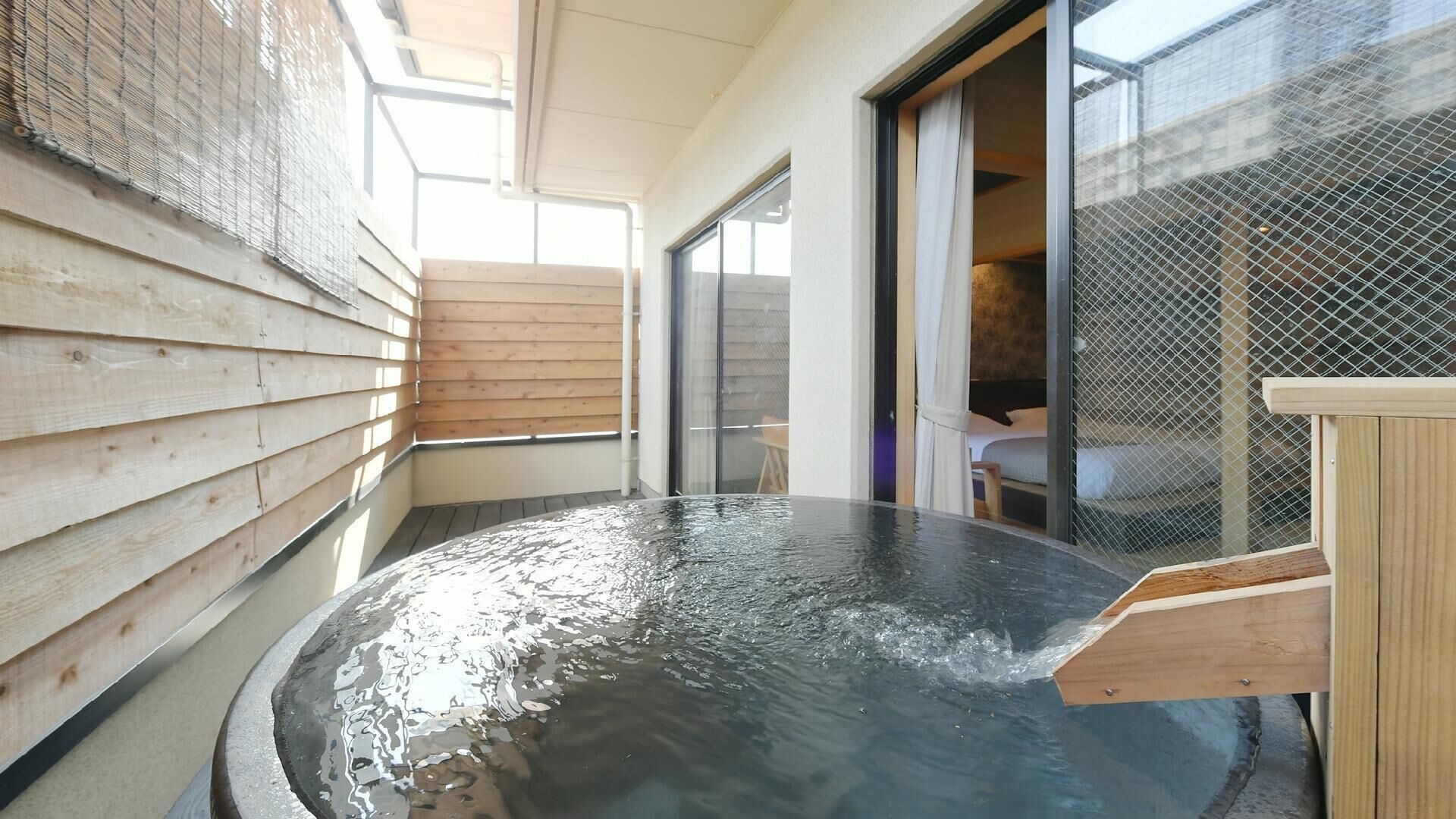 A hot spring bath with wooden walls and a glass door leading to a room.