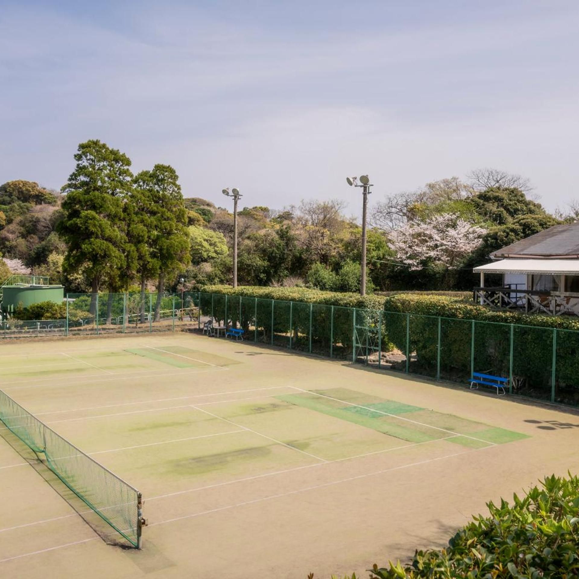 A tennis court with a net, surrounded by green fencing and trees.
