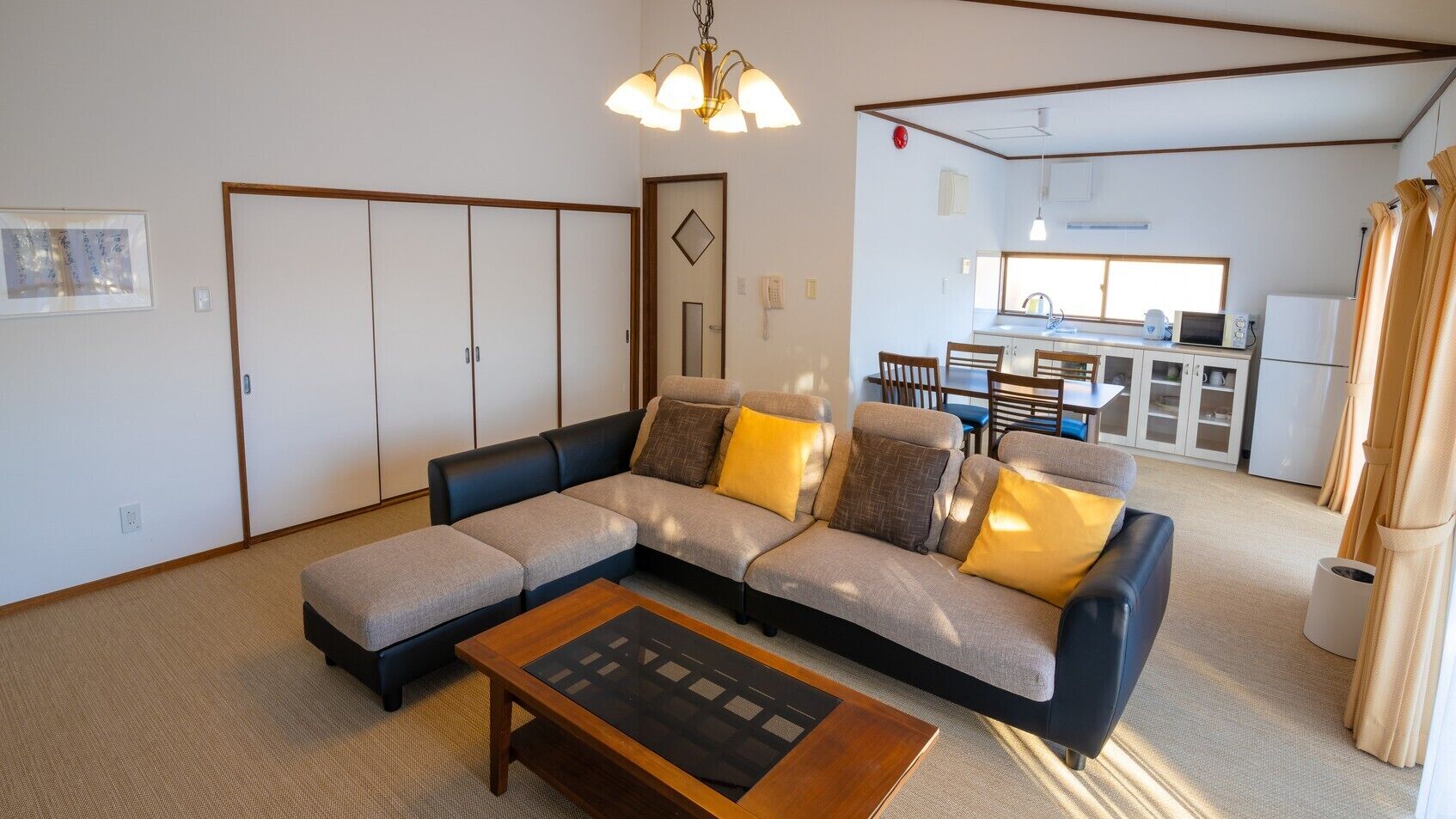 Uma sala de estar com sofá seccional, uma mesa de centro e uma cozinha ao fundo.