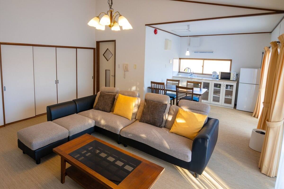 Ein Wohnzimmer mit einem Ecksofa, einem Couchtisch und einer Küche im Hintergrund.
