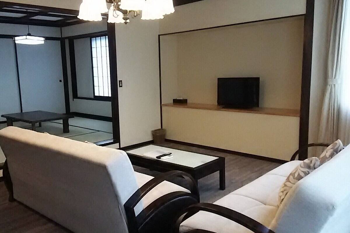 Ein Zimmer mit einer Couch, einem kleinen Tisch, einem Fernseher auf einem Regal und einer Schiebetür zu einem anderen Raum.