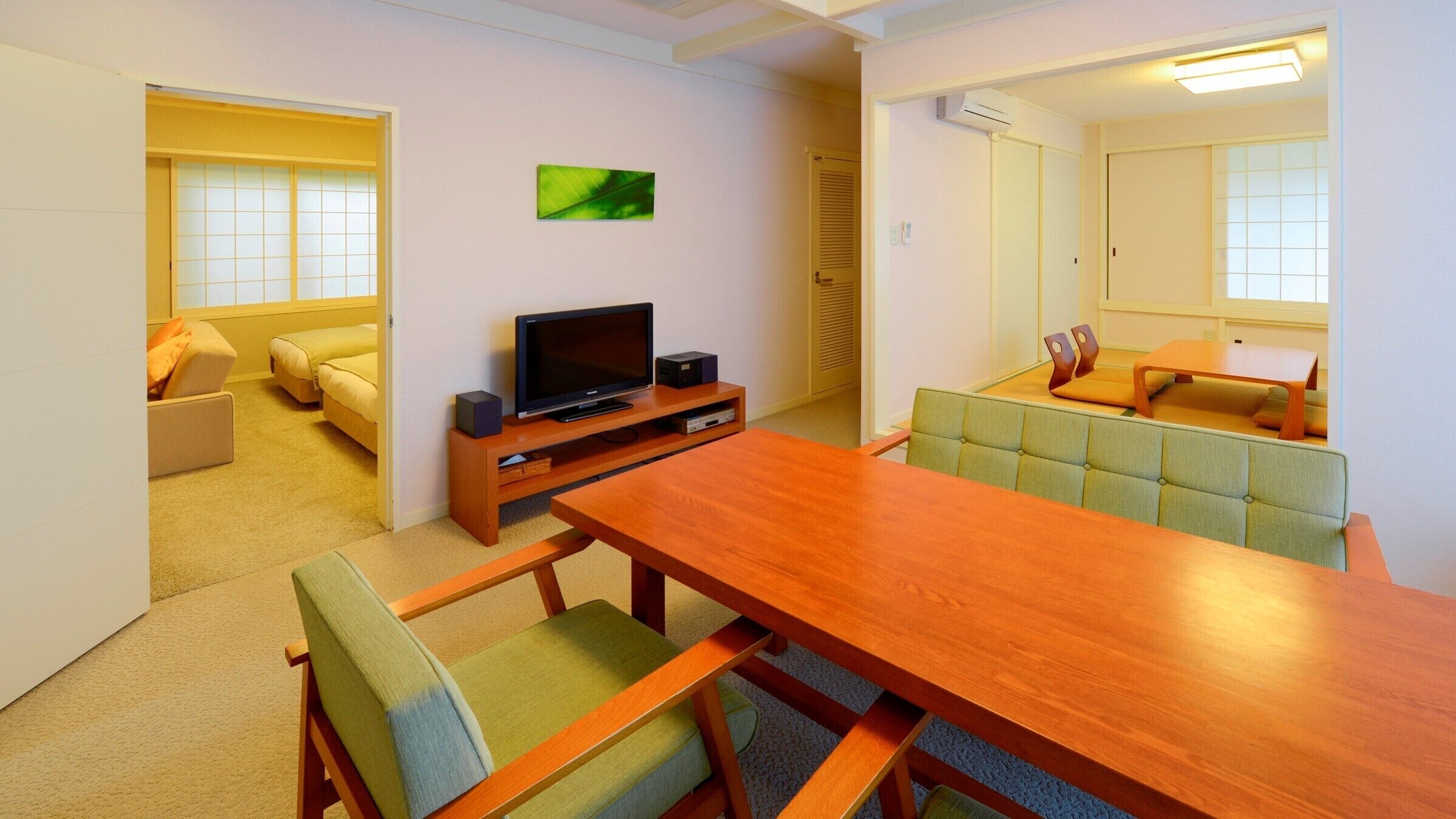 Uma sala de estar moderna com uma mesa de jantar de madeira, cadeiras estofadas em verde, uma TV de tela plana em um suporte de madeira, um sofá e um pequeno quadro verde na parede.