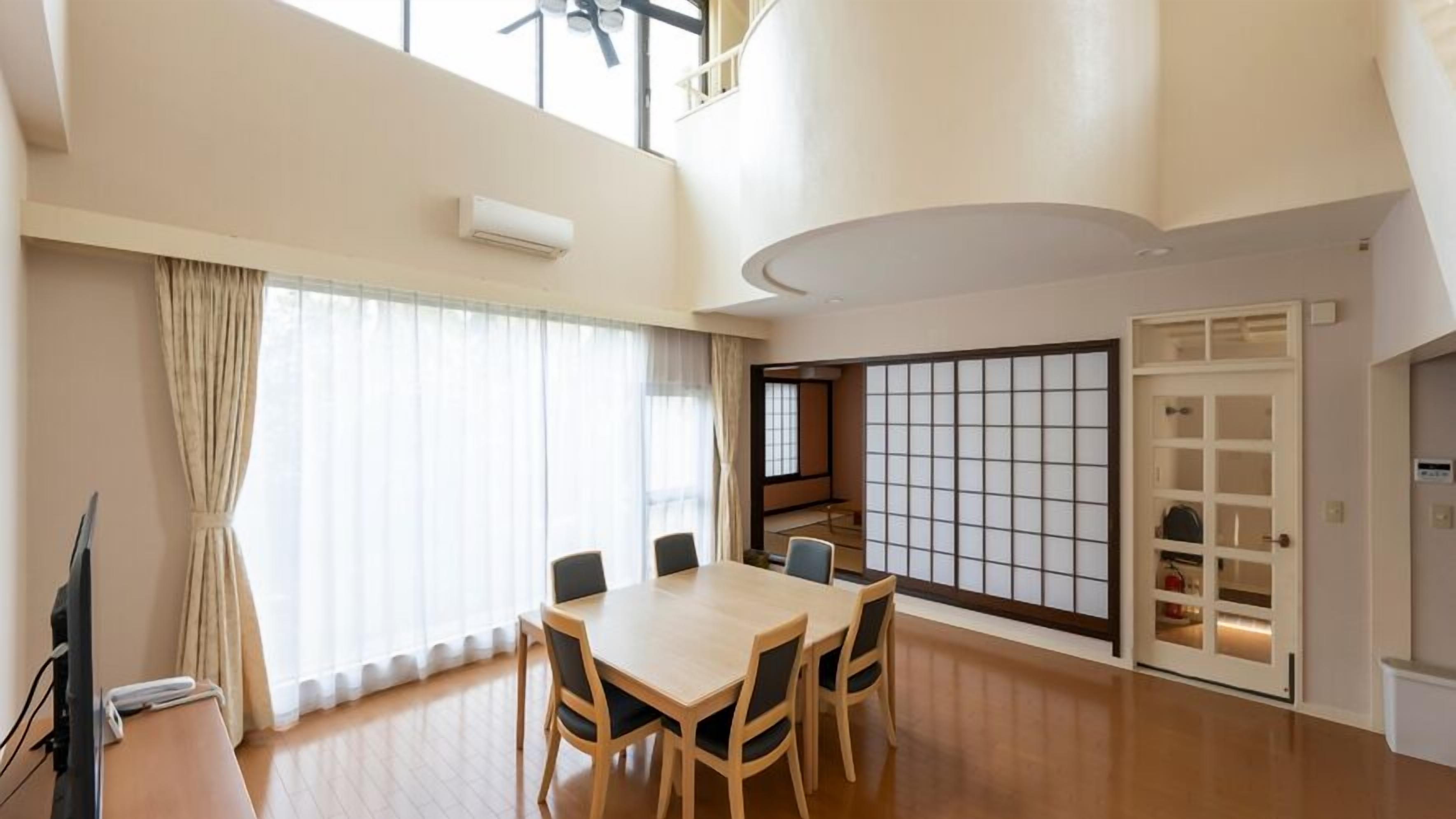 Quarto espaçoso com uma grande mesa de jantar, uma porta deslizante com padrão de grade e um ventilador de teto.