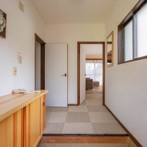 A hallway with a reception desk, a door, and a view into a living area with a sofa and a window. - Le Nessa Jogasaki (Ito)