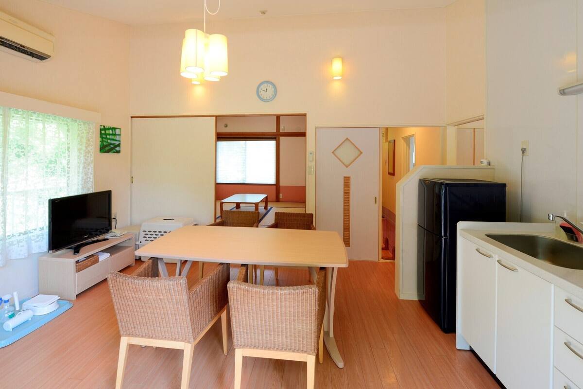 Ein kompakter Wohnbereich mit Esstisch, zwei Stühlen, Fernseher, Kühlschrank und Spüle.