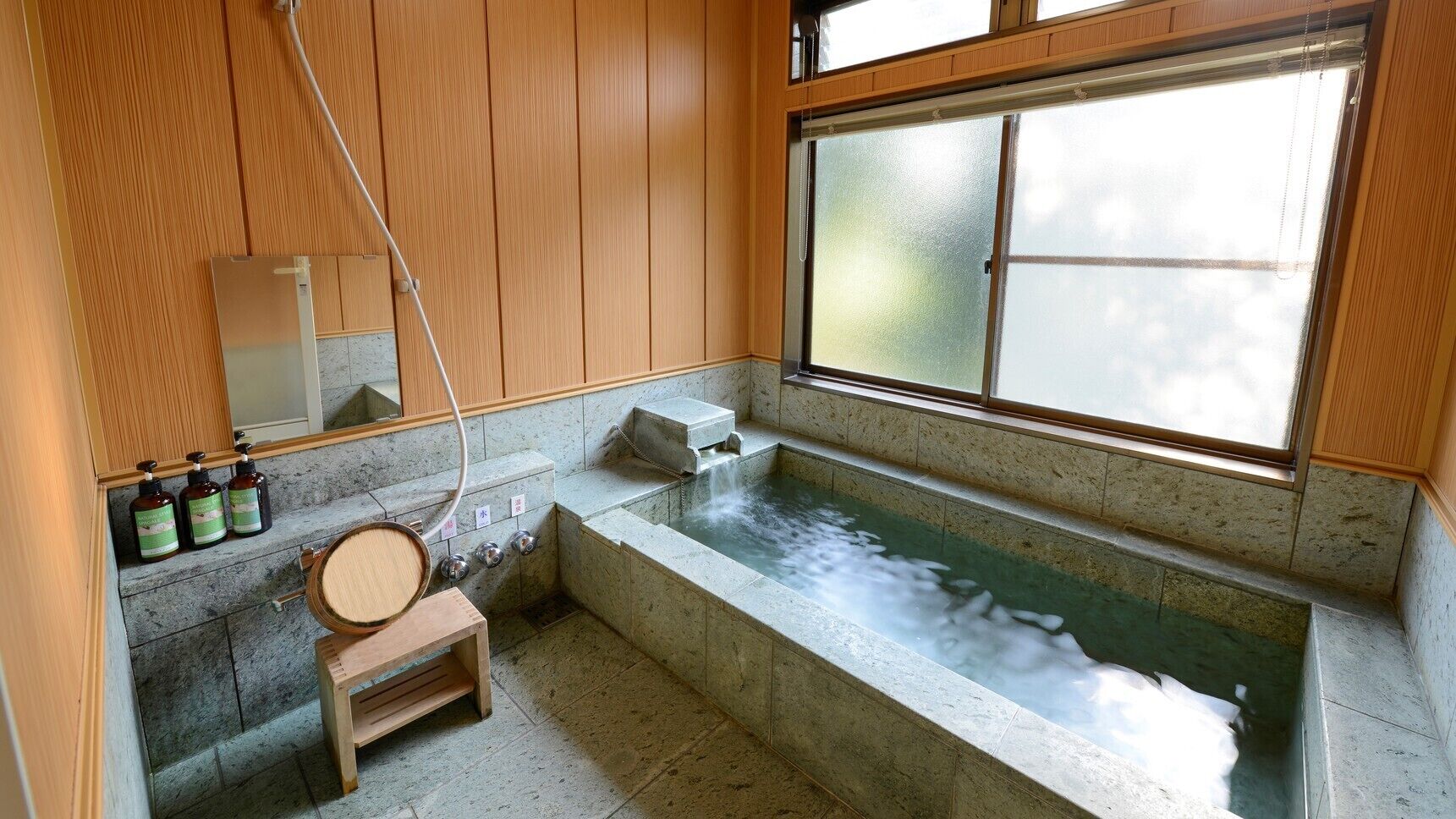 Uma onsen japonesa tradicional com um banco de madeira, uma banheira de pedra e uma janela com vista para o céu.
