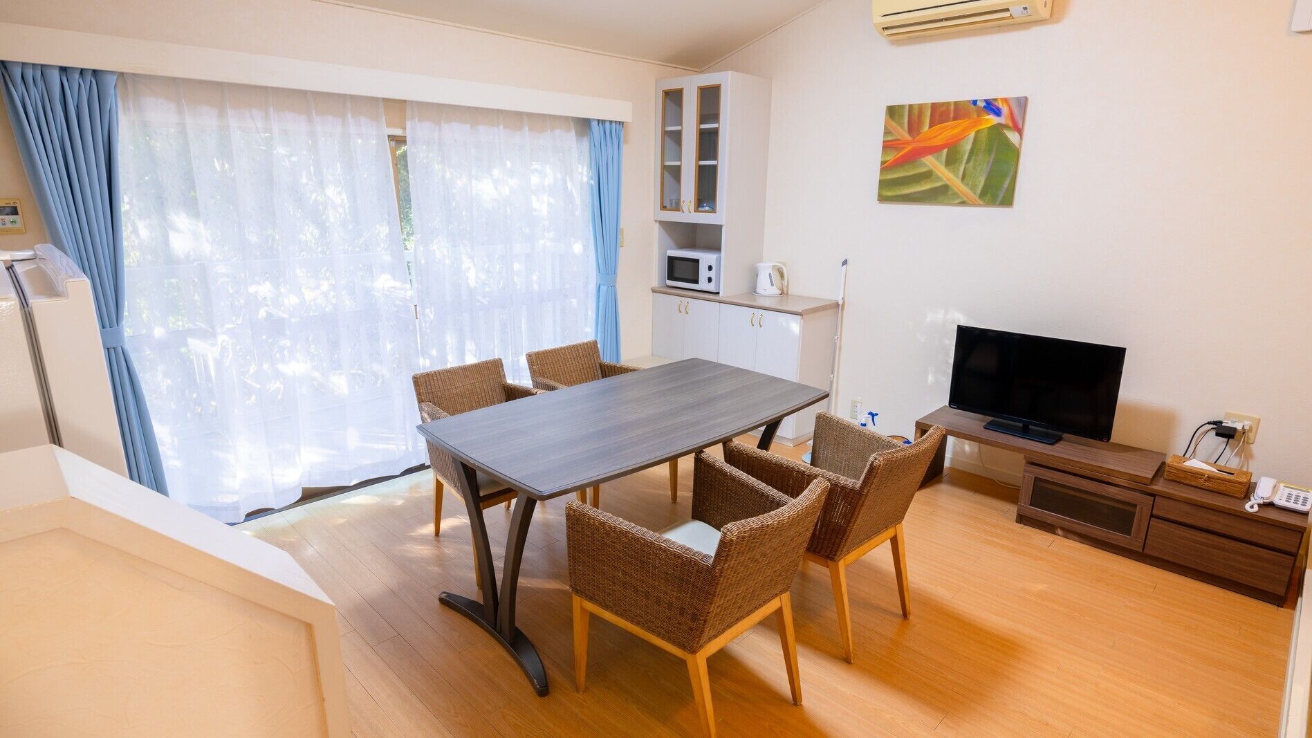 Uma sala de estar moderna com uma mesa de jantar, cadeiras de vime, uma televisão de tela plana, micro-ondas e um armário.