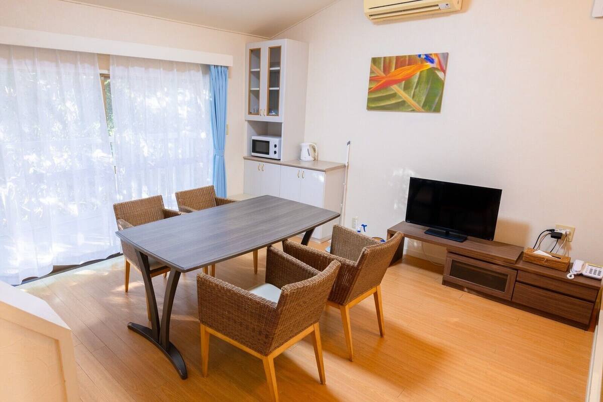 Ein modernes Wohnzimmer mit Esstisch, Korbstühlen, einem Flachbildfernseher, einer Mikrowelle und einem Schrank.