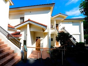 A multi-story building with a staircase leading to the entrance, a balcony, and a clear sky. - Le Nessa Jogasaki (Ito)
