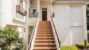 A building with a staircase leading to a door, surrounded by greenery.