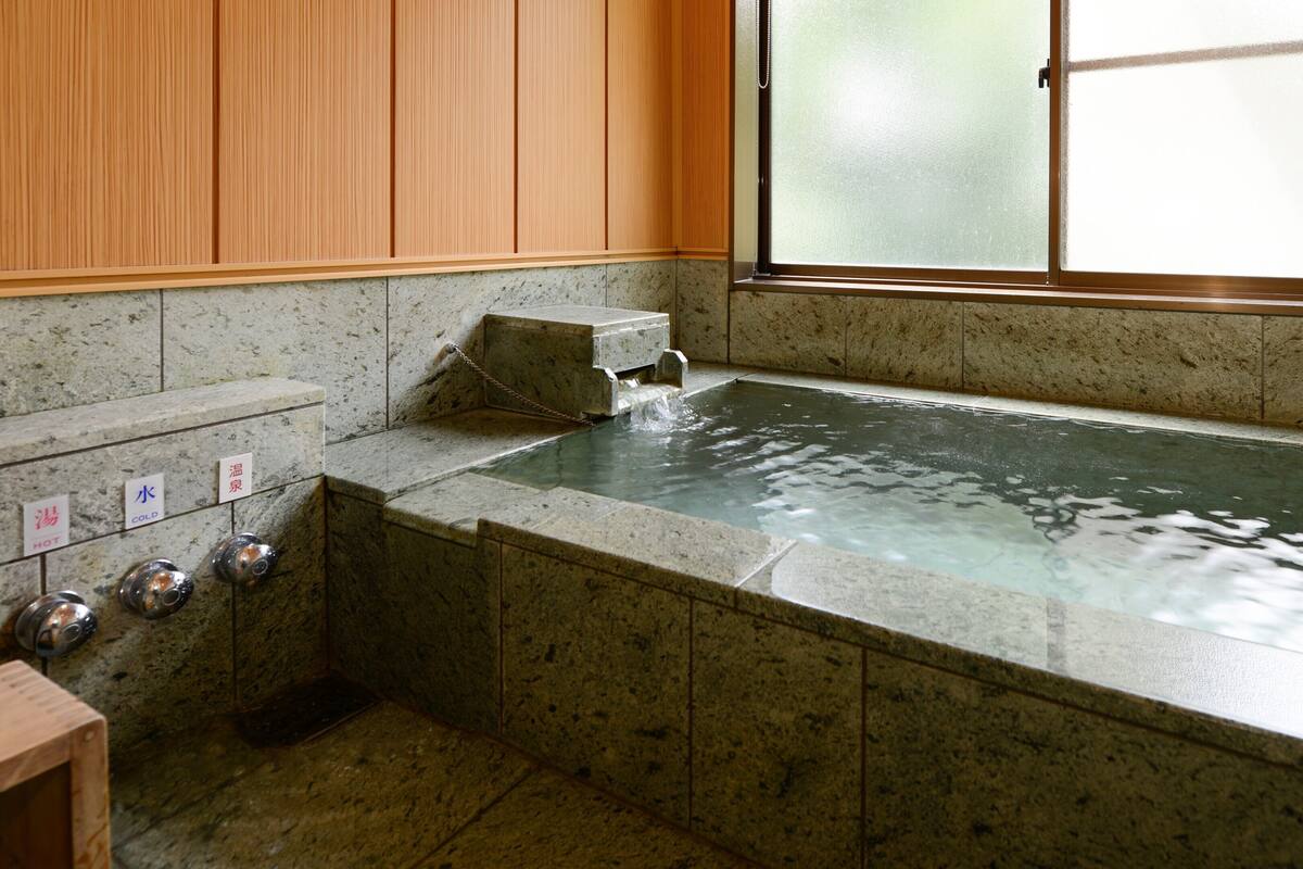 Eine Steinbadewanne mit einer Holzpaneelwand und einem Milchglasfenster.