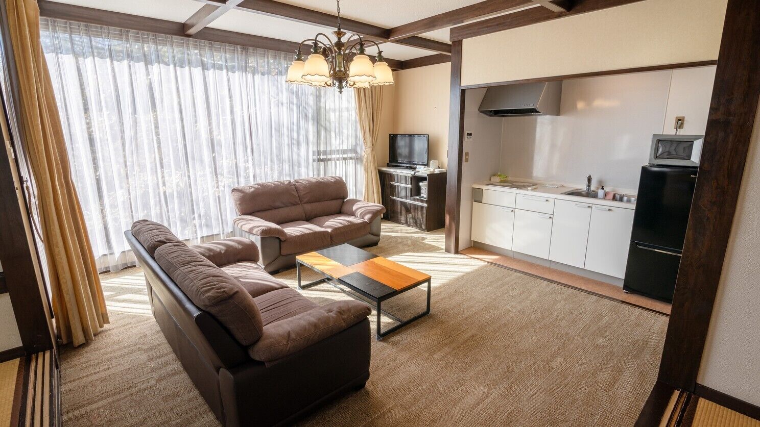 Ein Wohnzimmer mit einer Couch, einem Couchtisch und einem Fernseher. Es gibt eine Küchenzeile mit Schränken und einer Mikrowelle.