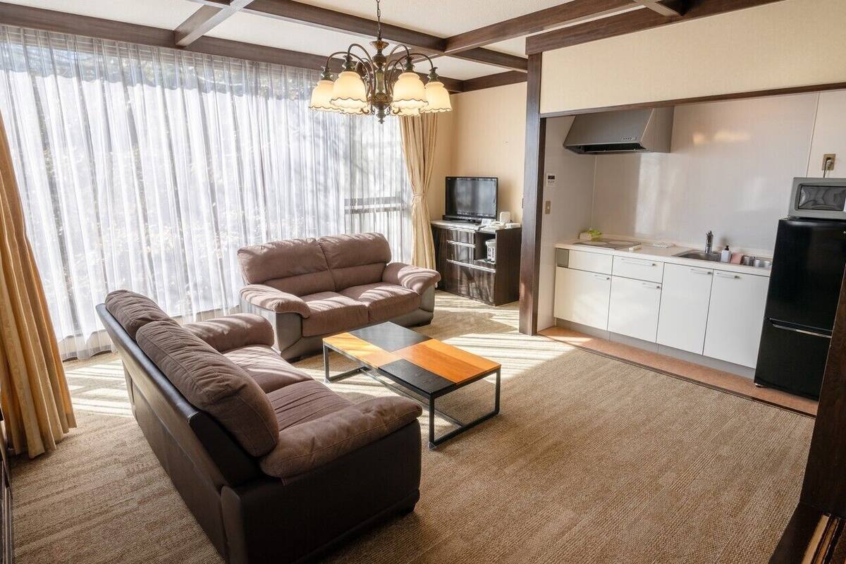 Ein Wohnzimmer mit einer Couch, einem Couchtisch und einem Fernseher. Es gibt eine Küchenzeile mit Schränken und einer Mikrowelle.