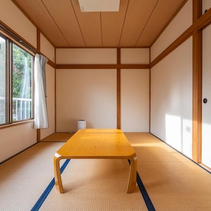A tatami room with a low wooden table, tatami mats, a sliding door, and a window with a view of greenery. - Le Nessa Jogasaki (Ito)