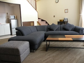 A living room with a sectional sofa, a coffee table, and a staircase. - Le Nessa Jogasaki (Ito)