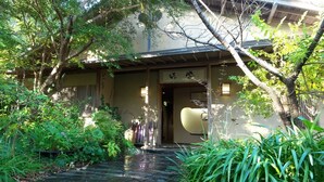 A traditional Japanese building with a covered entrance, a stone pathway, and lush greenery.