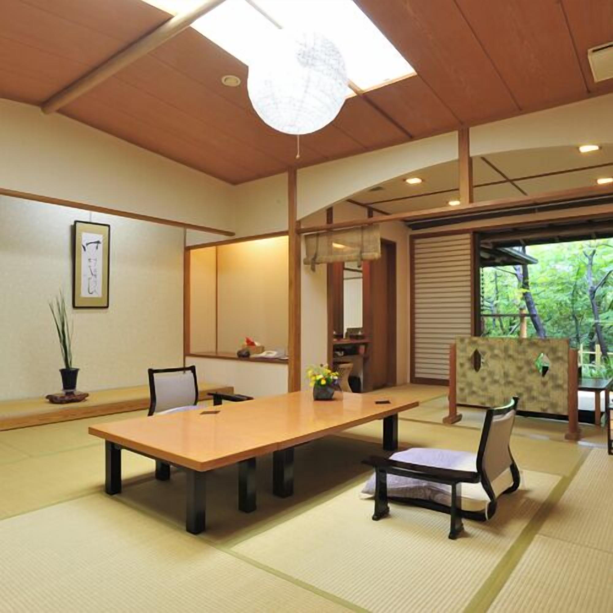 Una habitación tradicional japonesa con suelo de tatami, una mesa de madera, sillas, un panel shoji y vistas a la vegetación exterior.