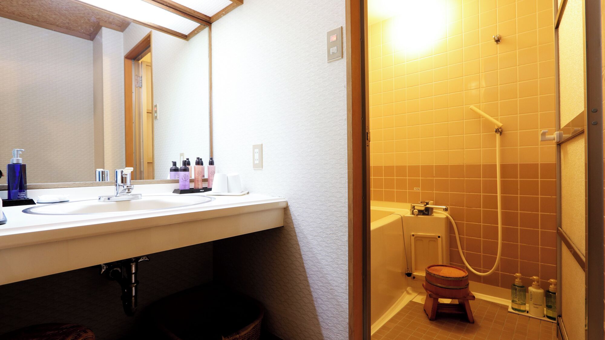 A bathroom with a white sink, mirror, and a shower area with a wooden stool.
