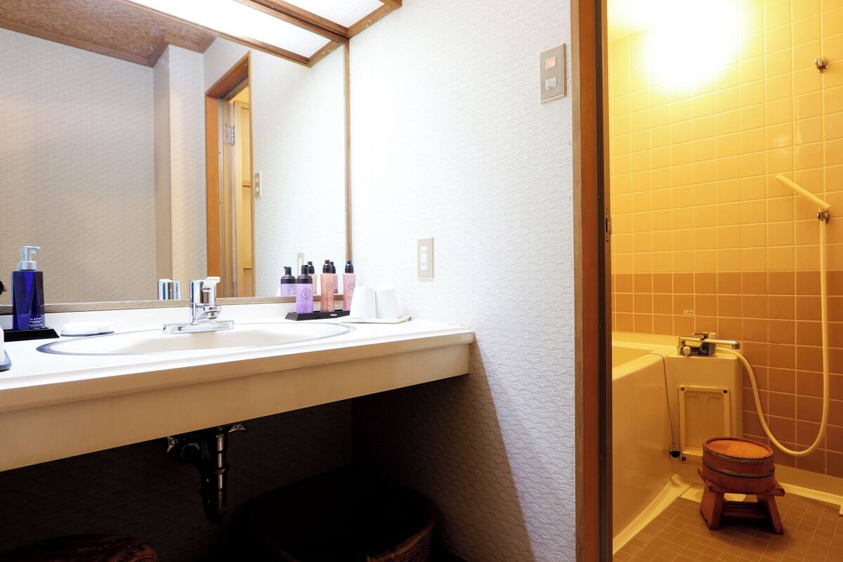A bathroom with a white sink, mirror, and a shower area with a wooden stool.