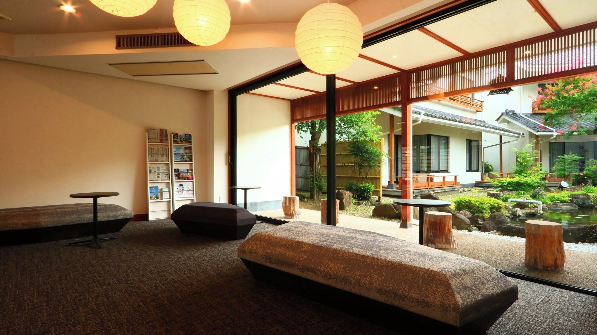 A room with a sofa, a small table, a bookshelf, and a view of a garden with a traditional building.