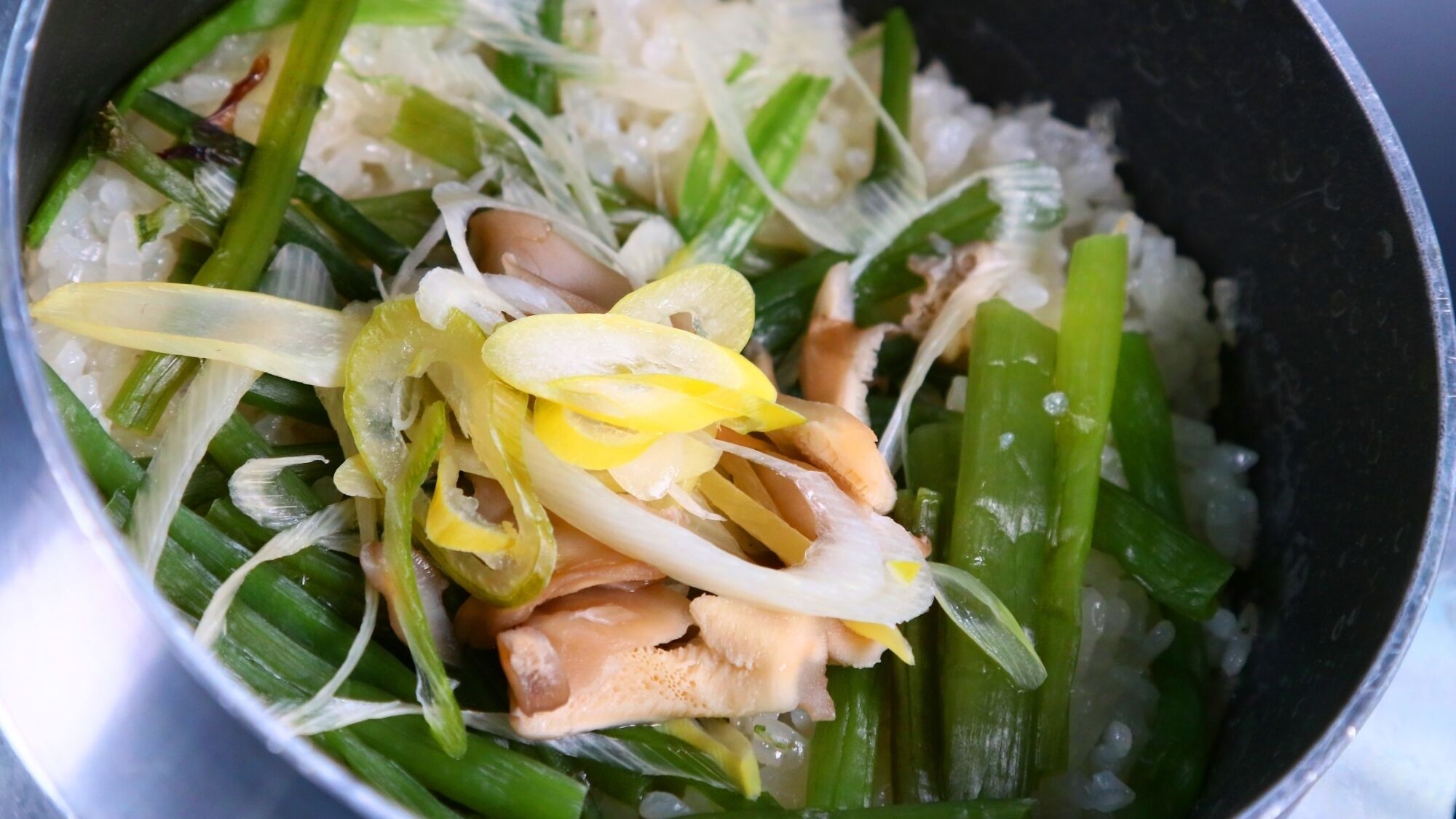 Un bol de riz accompagné de légumes verts et de tranches de fruits jaunes.