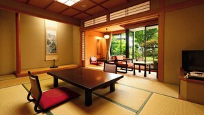 Una habitación japonesa tradicional con suelo de tatami, una mesa baja, sillas y un televisor.
