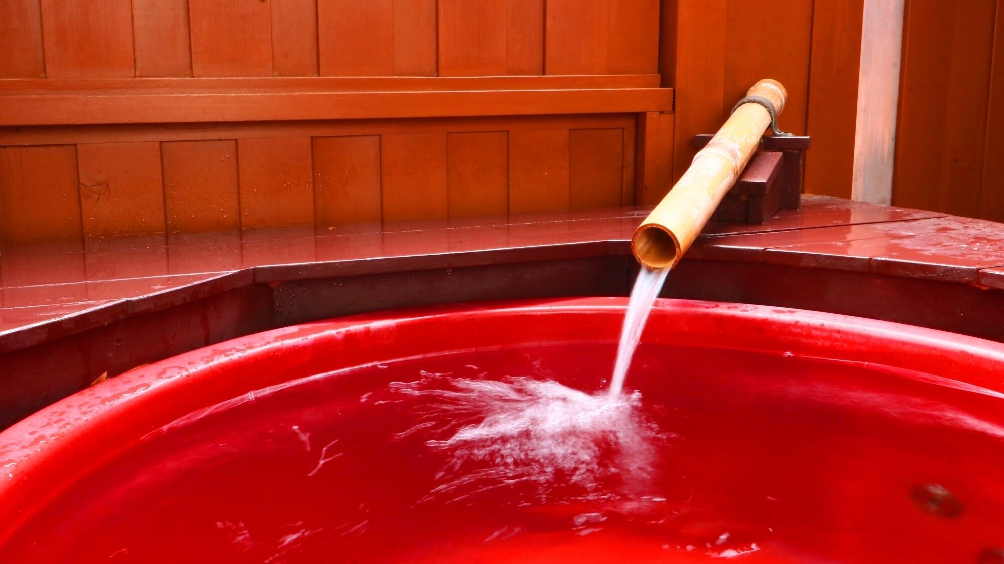 Eine rote Whirlwanne mit Bambusauslauf, im Hintergrund Holzverkleidung.