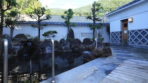 Un jardín japonés tradicional con un estanque de carpas, senderos de madera y un edificio con tejado de tejas.