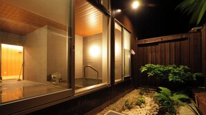 Un edificio moderno con fachada de vidrio, una zona de ducha visible y una valla de madera con plantas.