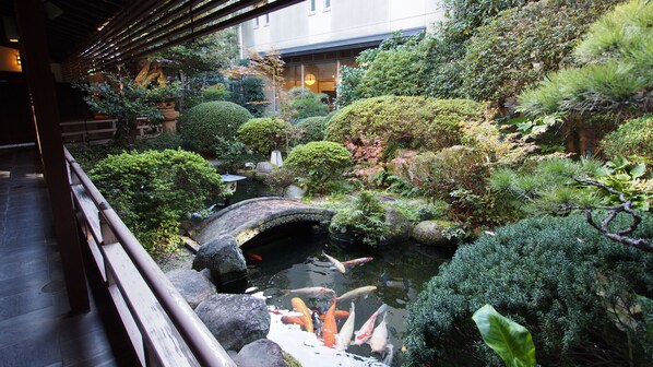 Un jardín japonés tradicional con estanque de carpas, puente de piedra y diversas plantas.