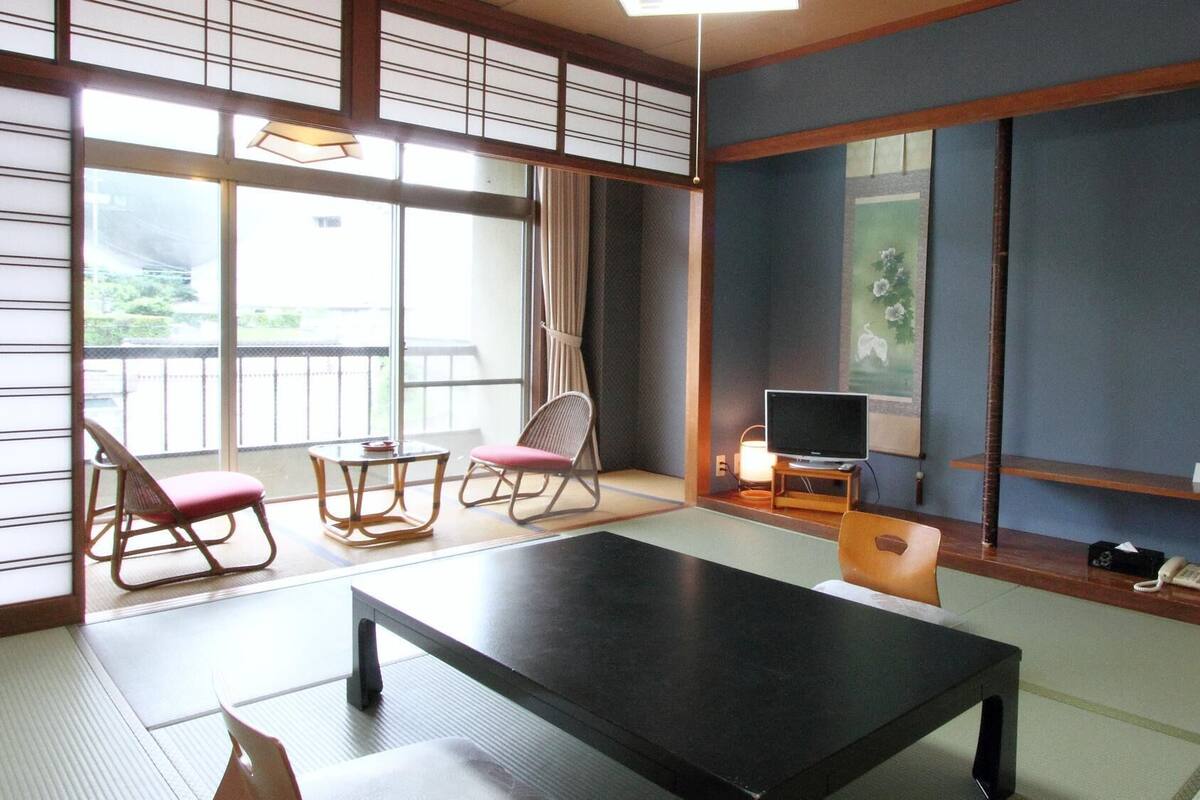 Une pièce de style japonais traditionnel, avec un sol recouvert de tatamis, une table basse, un téléviseur et une porte coulissante.