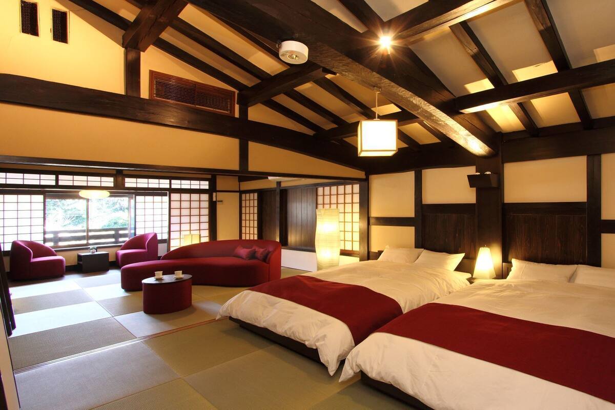 Une pièce de style japonais traditionnel, avec un sol recouvert de tatamis, un grand lit, deux fauteuils rouges et une petite table.