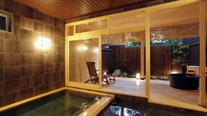 Ein Wellnessbereich mit Whirlpool, Holzterrasse und Blick auf den Garten.