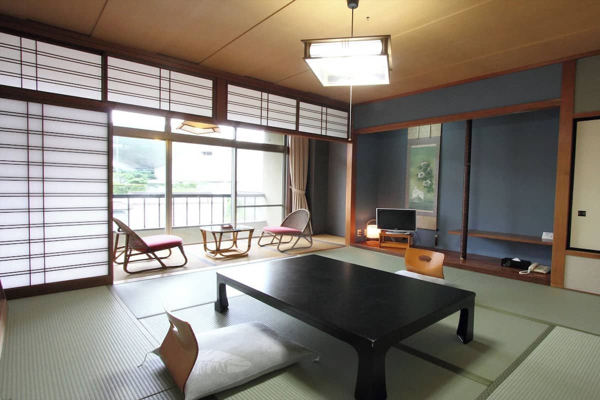 Ein traditioneller japanischer Raum mit Tatami-Boden, einem niedrigen Tisch, einem Fernseher und Blick ins Freie.
