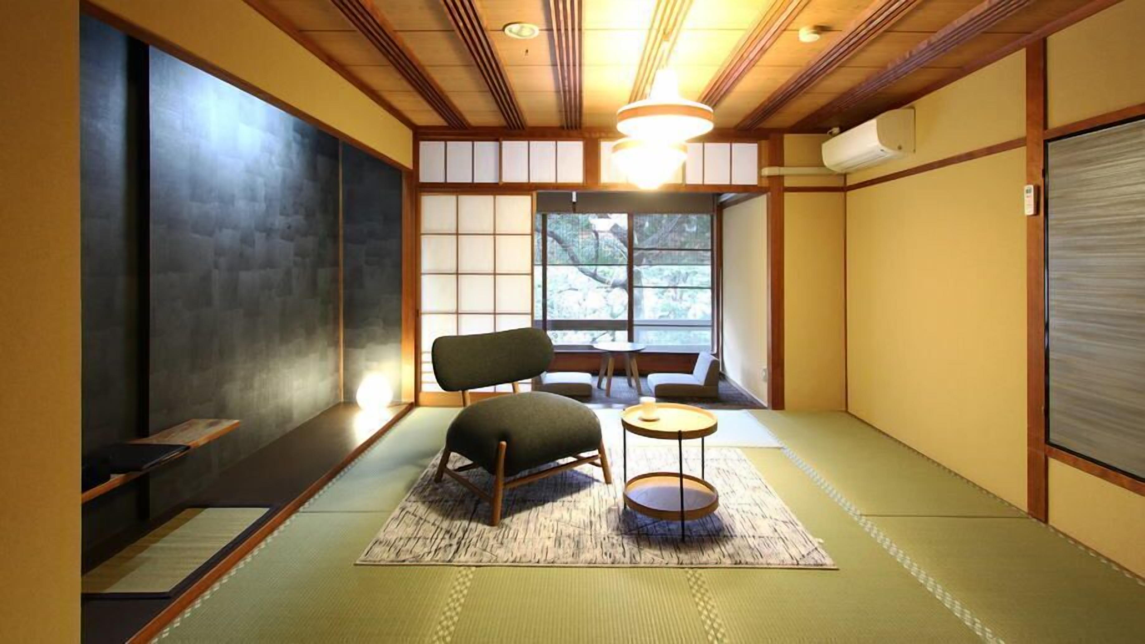 Una tradizionale stanza tatami con un tavolino, una sedia e una finestra che si affaccia su degli alberi.