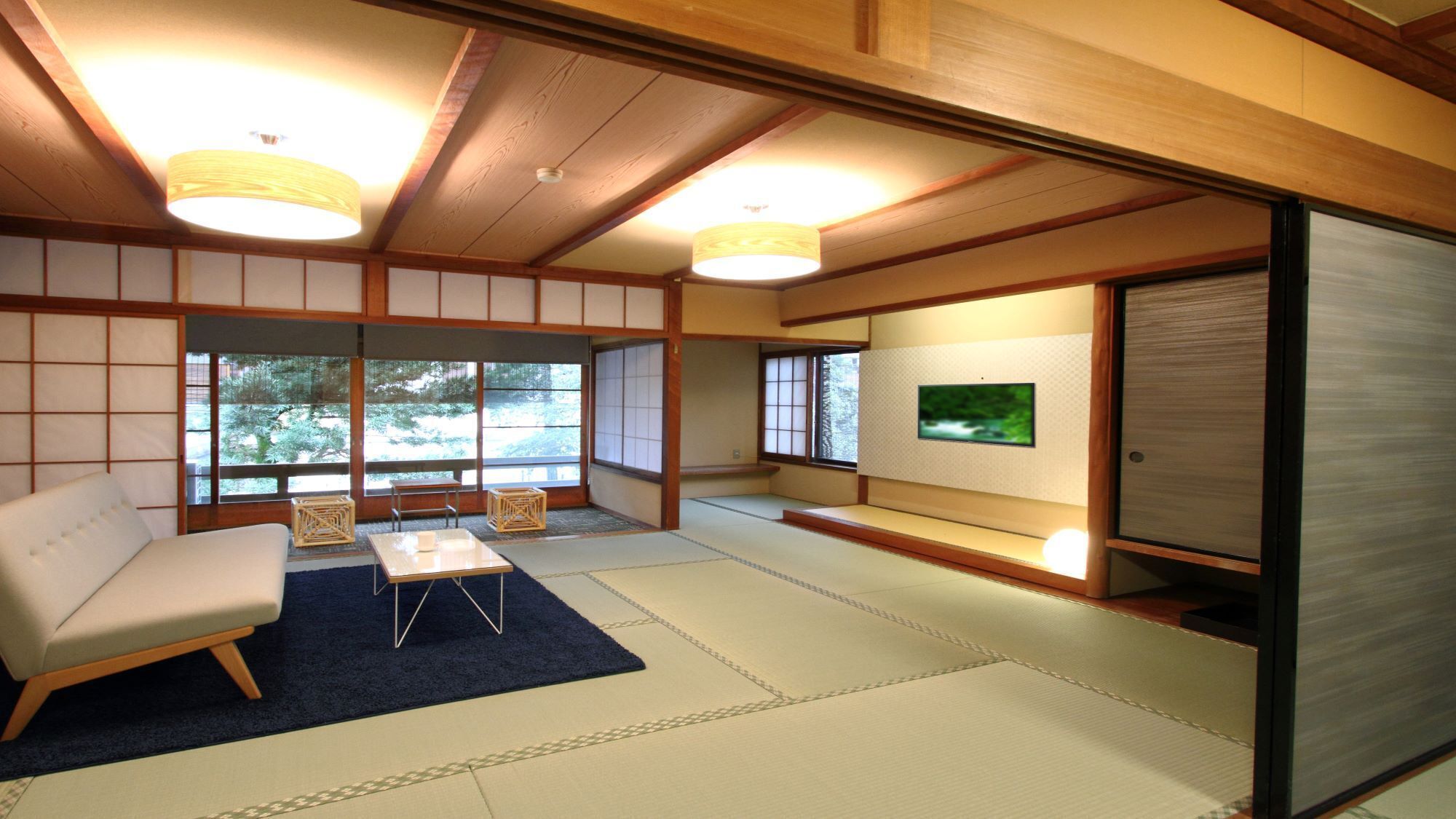 Una tradizionale stanza giapponese con pavimenti in tatami, un divano bianco, un tavolino e un televisore.