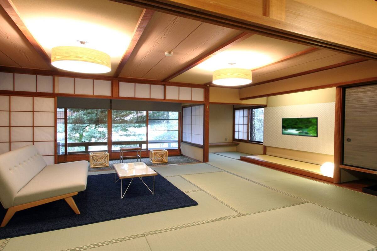 Une pièce de style japonais traditionnel, avec un sol recouvert de tatamis, un canapé blanc, une petite table et un téléviseur.