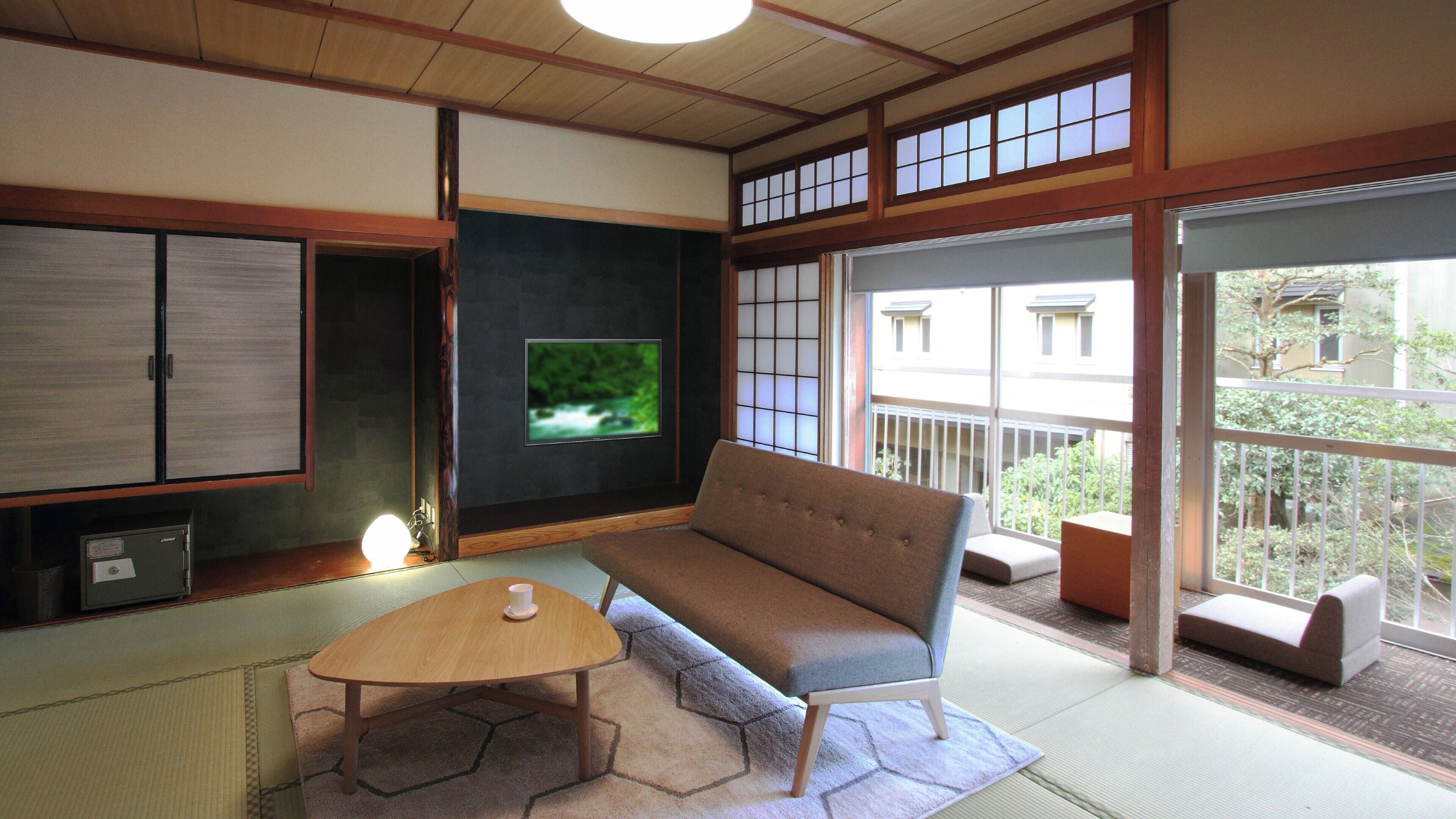 Una tipica stanza giapponese con pavimento in tatami, un tavolino, una poltrona, una TV, porte scorrevoli e vista all'esterno.