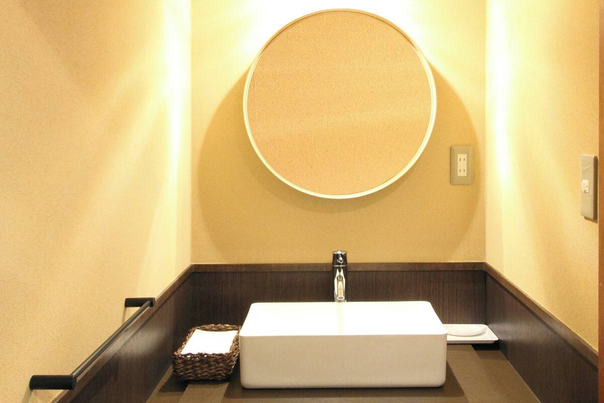 Une salle de bain avec un lavabo rectangulaire, un miroir rond et un luminaire fixé au mur.