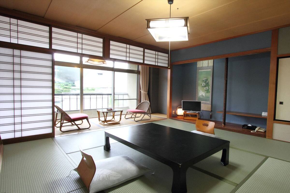 Une pièce de style japonais traditionnel, avec un sol recouvert de tatamis, une table basse, un téléviseur et des portes coulissantes.