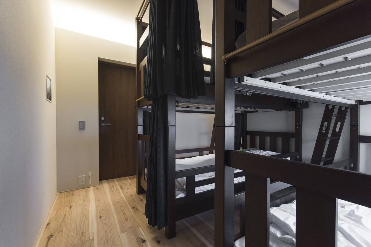 Een slaapkamer met een stapelbed, houten vloer, een deur en lichtschakelaar.