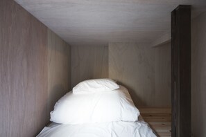 Una habitación estrecha, con paneles de madera y una cama apoyada en la pared.
