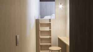 Une petite pièce comprenant un lit superposé, un petit tabouret et une étagère.