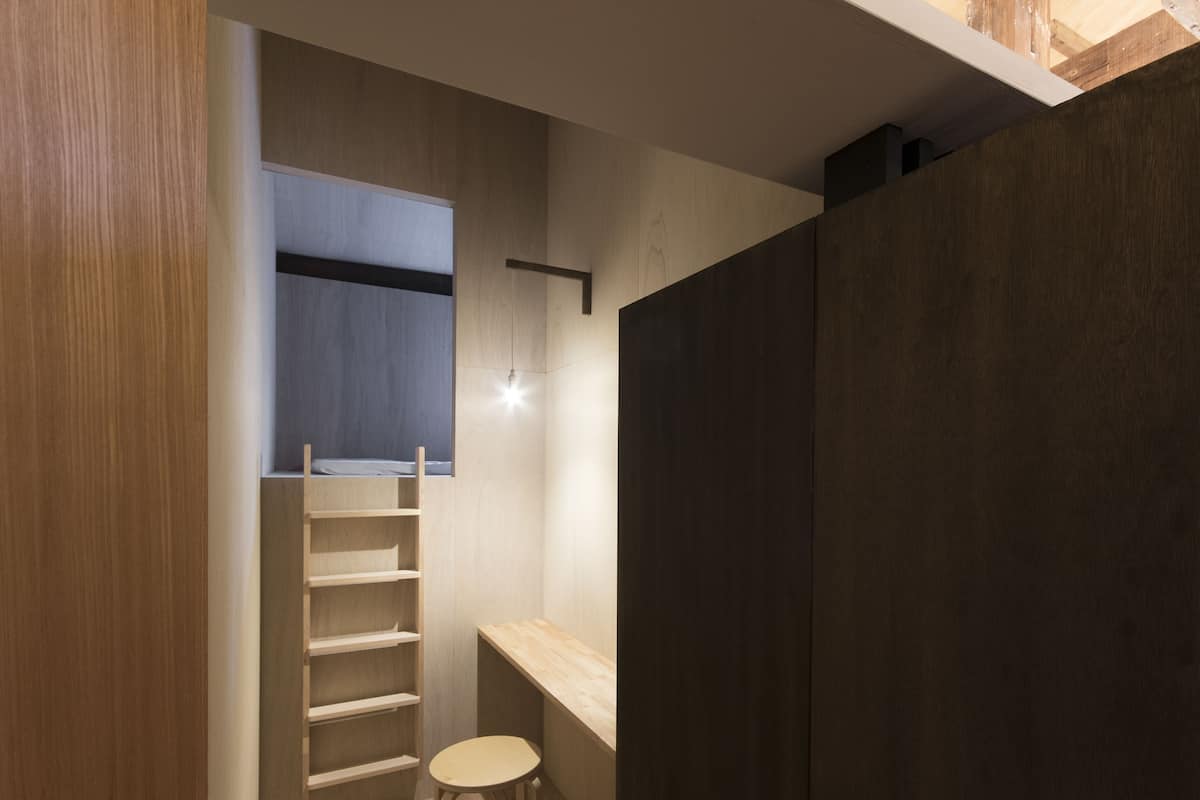 Een compacte kamer met een houten vloer, een ingebouwde bank, een ladder en een klein krukje.